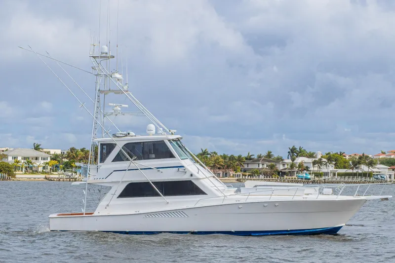 The Image of 1995 Viking 58 Convertible yacht cruising near coastal homes under cloudy skies. - 0