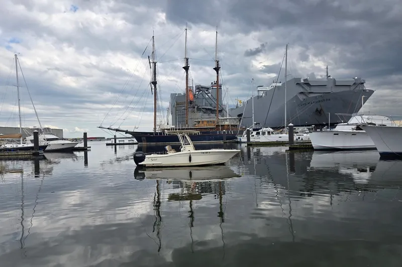 Slide: The Image of 2023 Scout 215 XSF boat in a marina with historic ships and cloudy sky. - 6
