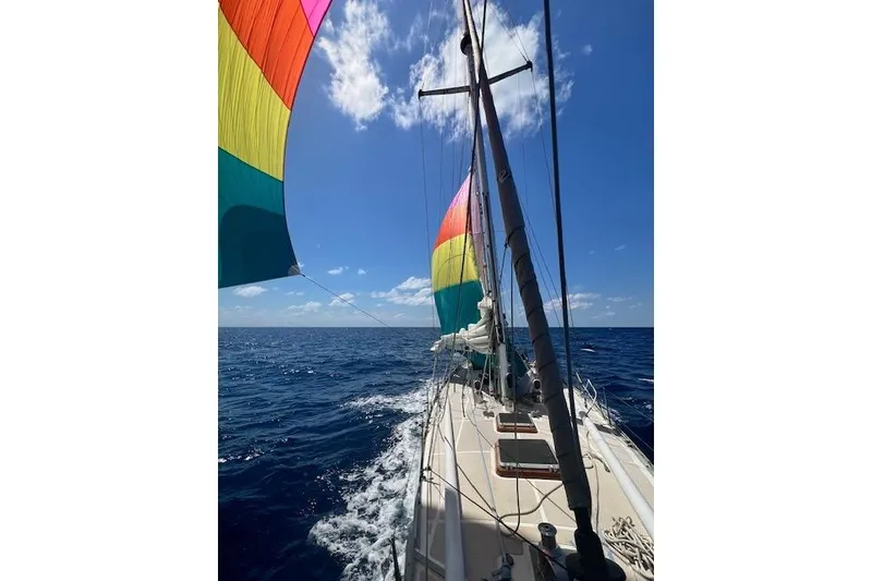 Slide: The Image of Sailing on a 1985 Robert Clark Ketch with colorful sails under a clear blue sky. - 10