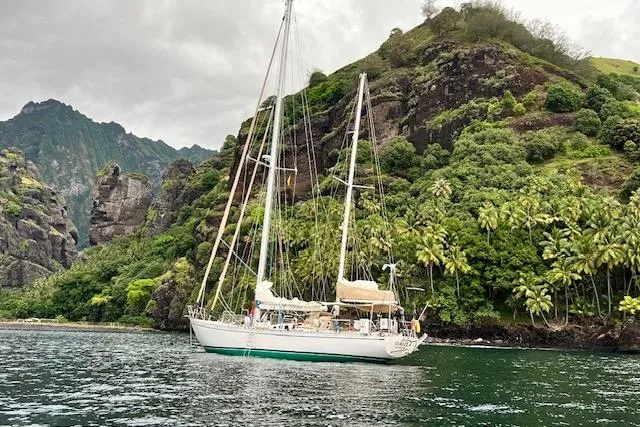 Slide: The Image of Sailboat "Robert Clark Ketch 1985" anchored near lush, rocky island coastline. - 67