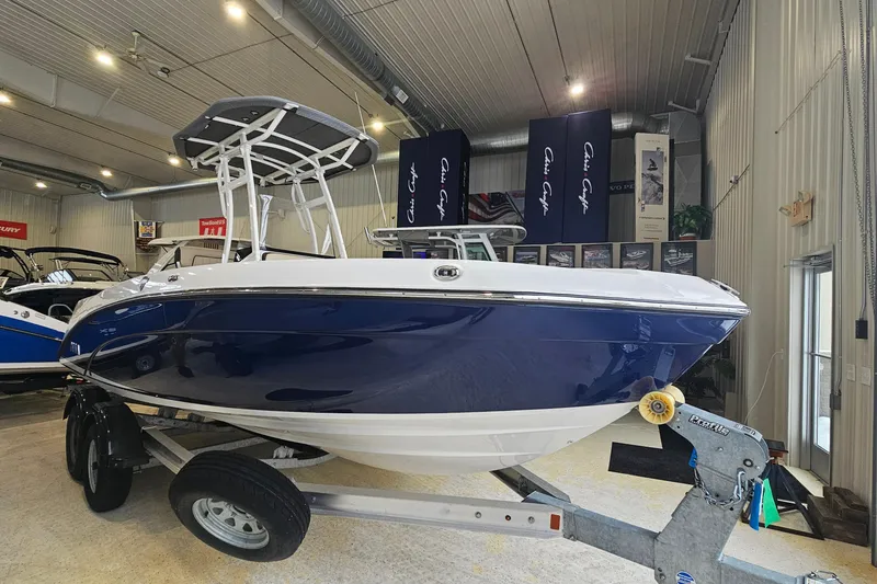 Slide: The Image of 2021 Yamaha Boats 210 FSH Sport in showroom, blue and white hull on trailer. - 1