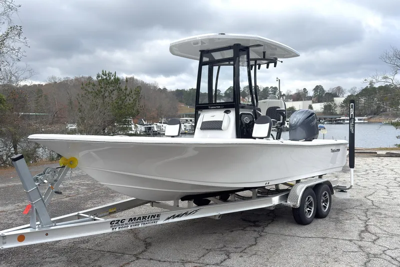 Slide: The Image of 2026 Tidewater 2210 Carolina Bay boat on trailer, parked near a lake under cloudy skies. - 5