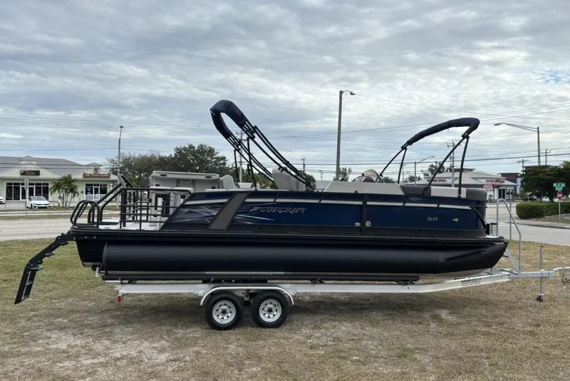 Slide: The Image of 2026 Starcraft SLS 3DL DH BAR pontoon boat on trailer, parked outdoors. - 2
