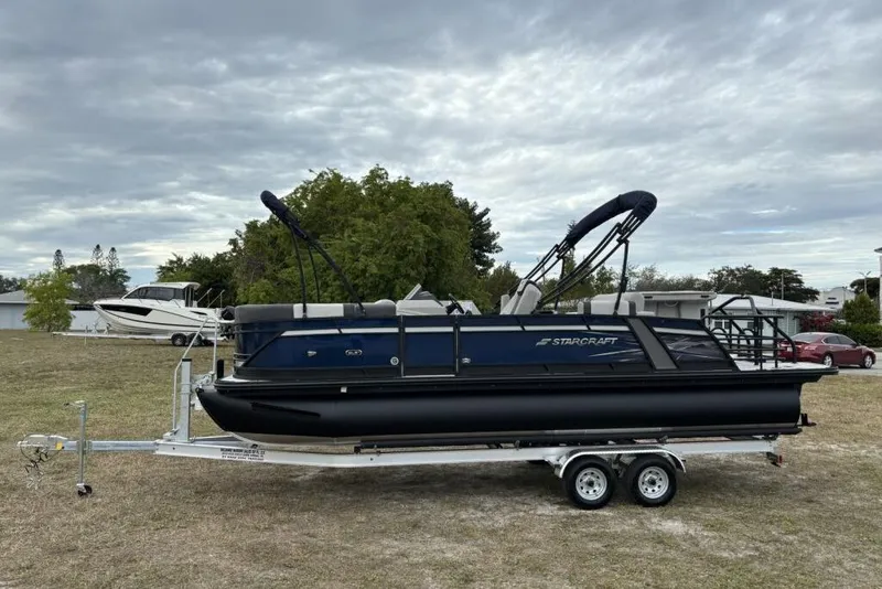 Slide: The Image of 2026 Starcraft SLS 3DL DH BAR pontoon boat on trailer, parked on grass under cloudy sky. - 5