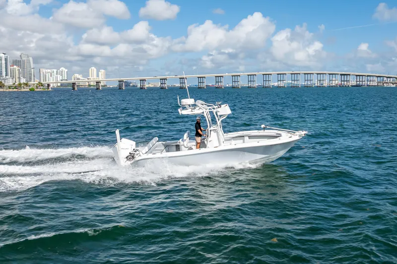 Slide: The Image of 2021 Yellowfin 26 Hybrid boat cruising on blue water near a city skyline and bridge. - 12