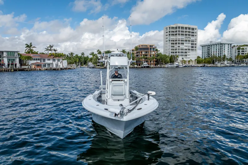 Slide: The Image of 2021 Yellowfin 26 Hybrid boat cruising on a scenic waterfront with buildings in the background. - 2