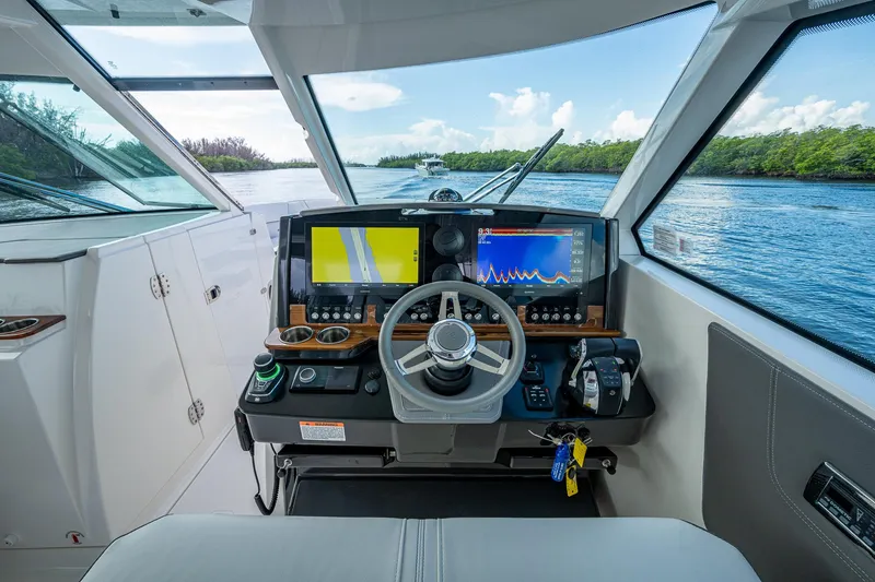 Slide: The Image of 2021 Tiara Yachts 38 LX helm with navigation screens and steering wheel on a scenic waterway. - 19