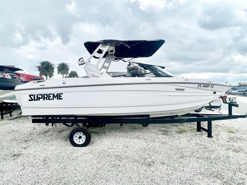 The Image of 2023 Supreme S220 boat on trailer, white exterior, black canopy, parked outdoors. - 0