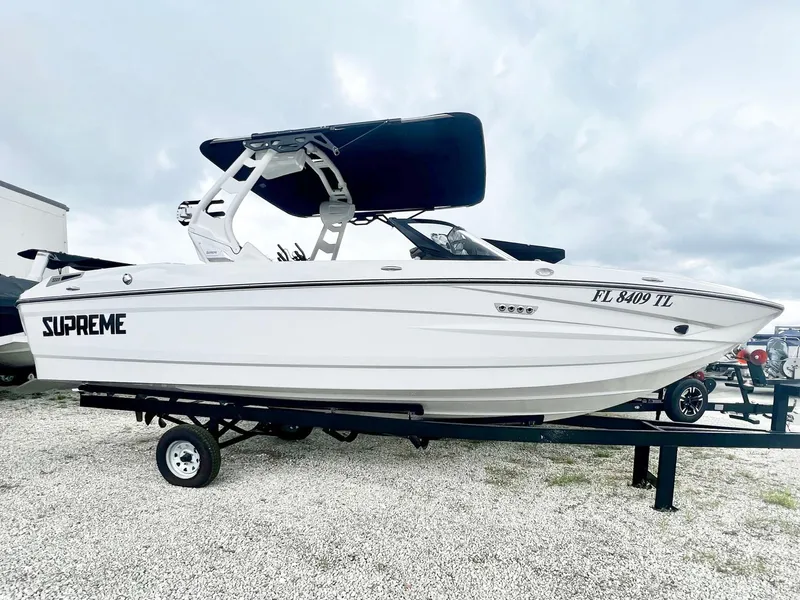 Slide: The Image of 2023 Supreme S220 boat on trailer, white exterior, black canopy, side view. - 1