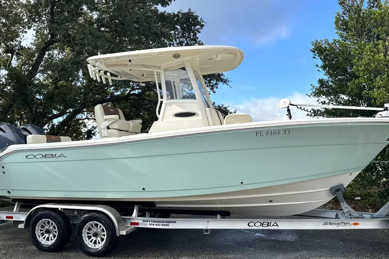 The Image of 2023 Cobia 240 Center Console boat on trailer, light blue hull, parked outdoors. - 0