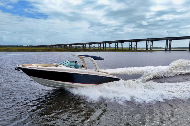 Slide: The Image of 2020 Chris-Craft Launch 31 GT cruising on water near a bridge under a cloudy sky. - 11