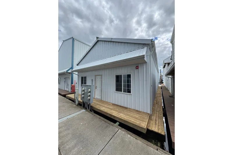 Slide: The Image of 2005 Larson Boat House, 60-foot model, with metal siding and wooden dock, under cloudy sky. - 4