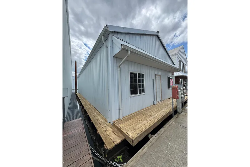 Slide: The Image of 2005 Larson Boat House, 60-foot model, with wooden dock and metal siding under cloudy sky. - 6