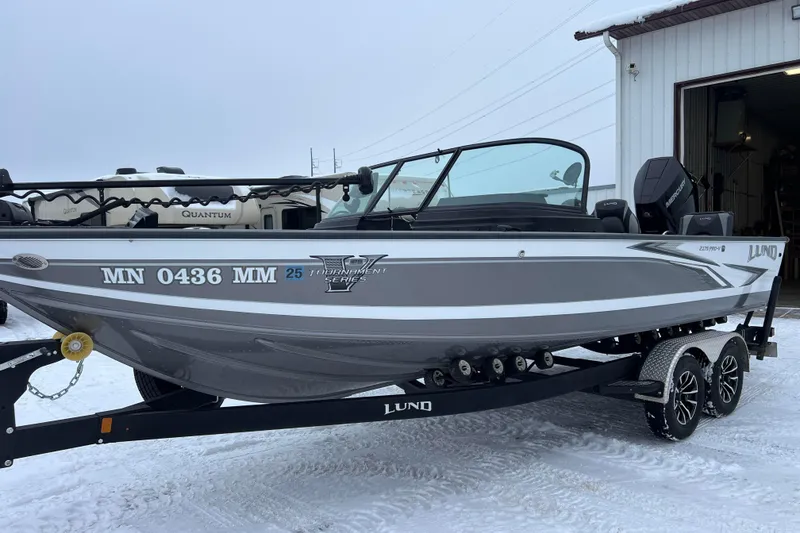 The Image of 2023 Lund 2175 Pro-V boat on trailer by a lake, featuring sleek design and modern features. - 0