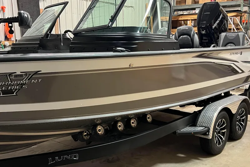 Slide: The Image of 2023 Lund 2175 Pro-V boat in a garage, showcasing sleek design and dual-axle trailer. - 46