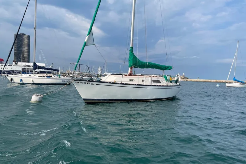 The Image of 1978 Hunter 30 sailboat anchored in a marina with other boats and a cityscape background. - 0