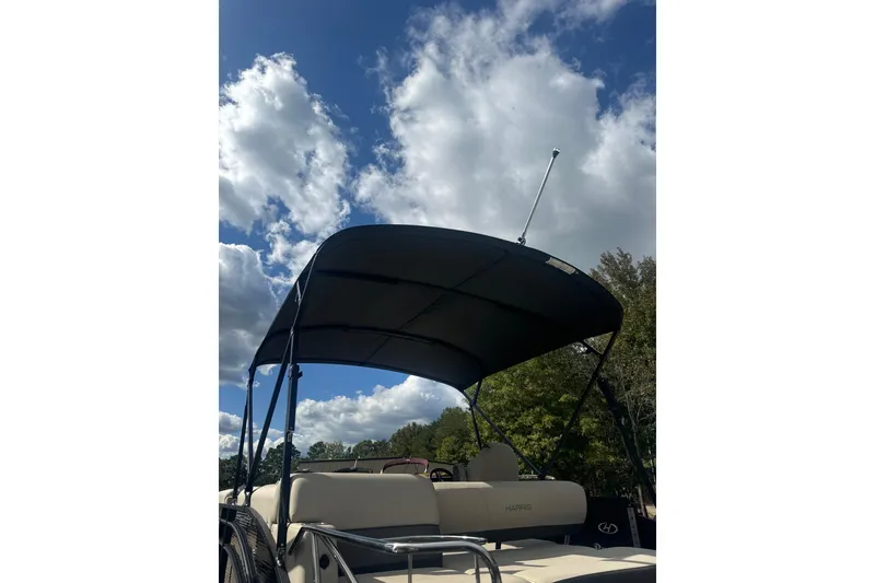 Slide: The Image of 2023 Harris HCX 230 Swingback boat with canopy under a partly cloudy sky. - 23