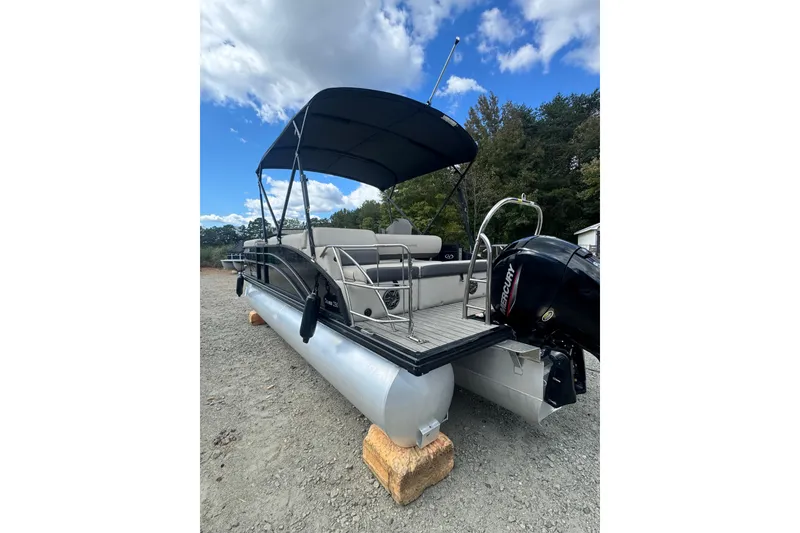 Slide: The Image of 2023 Harris HCX 230 Swingback pontoon boat with canopy and outboard motor, parked on gravel. - 7