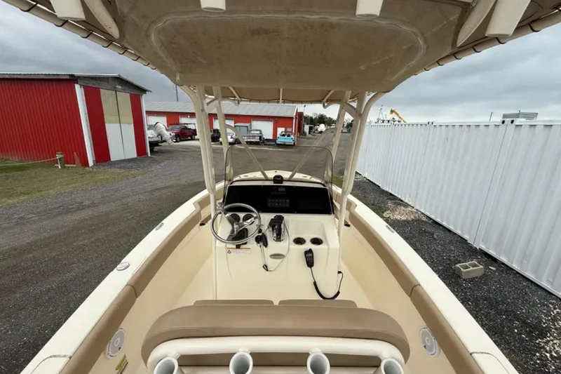 Slide: The Image of 2023 Scout 215 XSF boat interior with steering console and seating, parked near red and white buildings. - 7