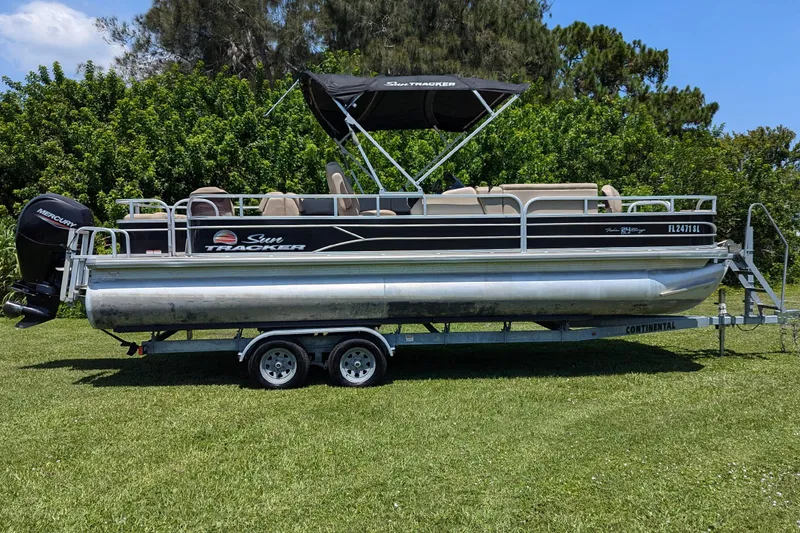 Slide: The Image of 2019 Sun Tracker Fishin' Barge 24 DLX pontoon boat on trailer, parked on grass. - 2