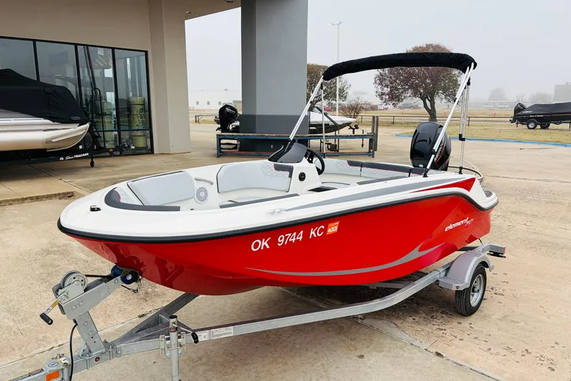 Slide: The Image of 2023 Bayliner Element M15 boat in vibrant red on a trailer, parked outdoors. - 4