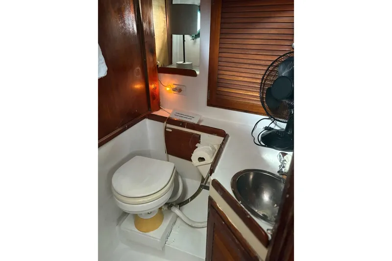 Slide: The Image of 1972 Islander 40MS yacht bathroom with toilet, sink, fan, and wooden accents. - 12