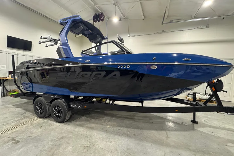 Slide: The Image of 2026 Supra SL 450 boat in showroom, sleek blue and black design on trailer. - 0