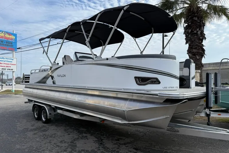 Slide: The Image of 2026 Avalon LSZ Versatile Rear Bench Windshield pontoon boat on trailer, parked outdoors. - 42