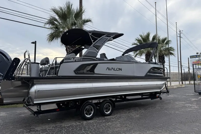 Slide: The Image of 2026 Avalon Excalibur LTD Quad Lounger Shift pontoon boat on trailer, parked outdoors. - 12