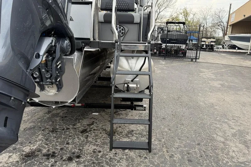 Slide: The Image of 2026 Avalon Excalibur LTD Quad Lounger Shift boat with ladder and motor, parked on pavement. - 13