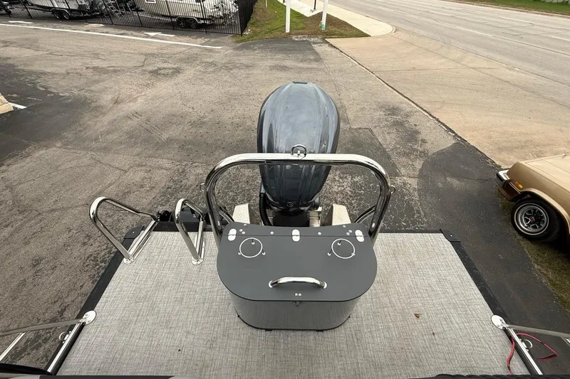 Slide: The Image of 2026 Avalon Excalibur LTD Quad Lounger Shift boat with outboard motor, parked on pavement. - 14