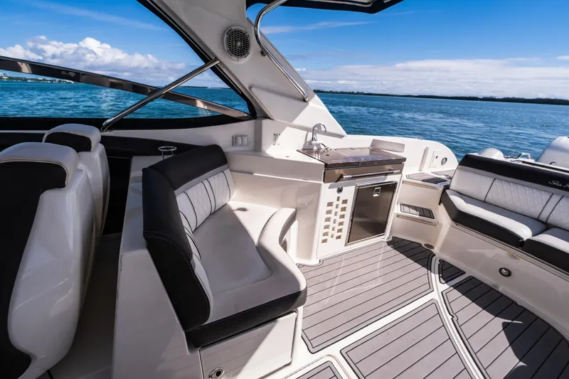 Slide: The Image of 2018 Sea Ray SLX 350 Outboard interior with seating and kitchenette, overlooking blue water. - 17