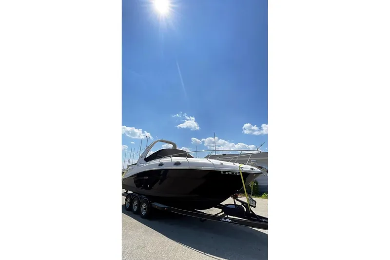 Slide: The Image of 2006 Sea Ray 260 Sundancer boat interior with white seating, near a house and trees. - 3