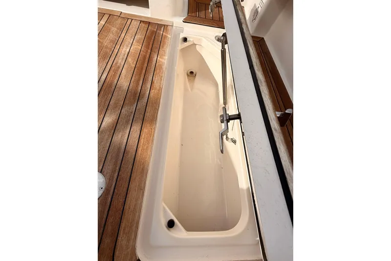 Slide: The Image of 2018 Pursuit DC 365 Dual Console boat storage compartment with wooden deck. - 52