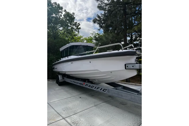 Slide: The Image of 2022 Axopar 28 AFT CABIN boat on trailer, surrounded by trees and cloudy sky. - 50
