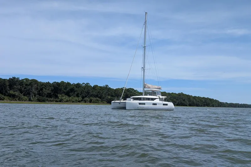 Slide: The Image of 2022 Lagoon 46 catamaran sailing on calm waters near a forested shoreline. - 124