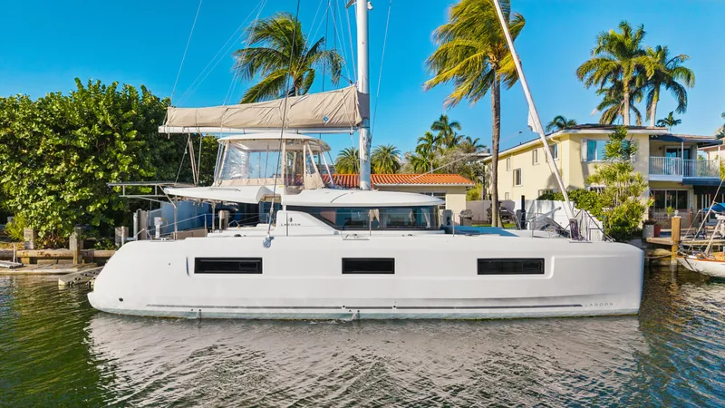 Slide: The Image of 2022 Lagoon 46 catamaran docked by palm trees and waterfront homes. - 2