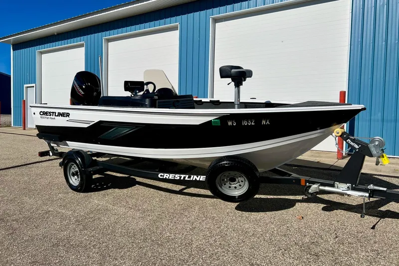 The Image of 2024 Crestliner 1650 Fish Hawk SC boat on trailer, parked outside blue building. - 0