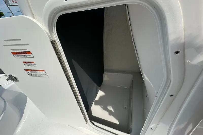 Slide: The Image of 2024 NauticStar 274 Bay boat storage compartment with open door and warning labels. - 7