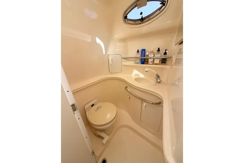 Slide: The Image of 2001 Sea Ray 340 Sundancer bathroom with toilet, sink, and toiletries under a porthole window. - 21