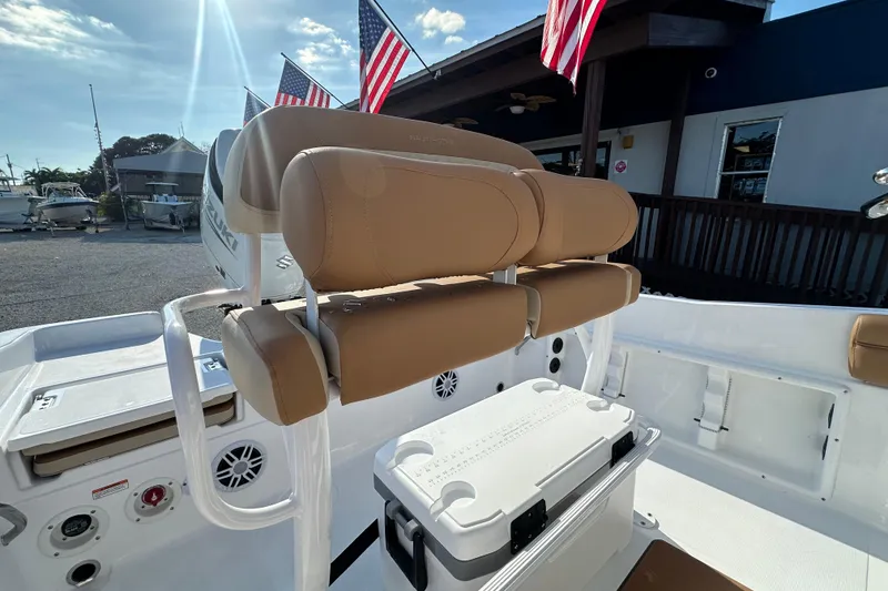 Slide: The Image of 2025 NauticStar 231 Hybrid boat interior with tan seating and cooler, American flags in background. - 12