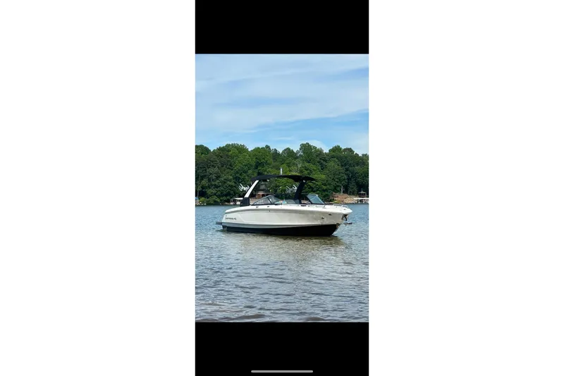 Slide: The Image of 2021 Chaparral 26 Surf boat on a calm lake with trees in the background. - 15