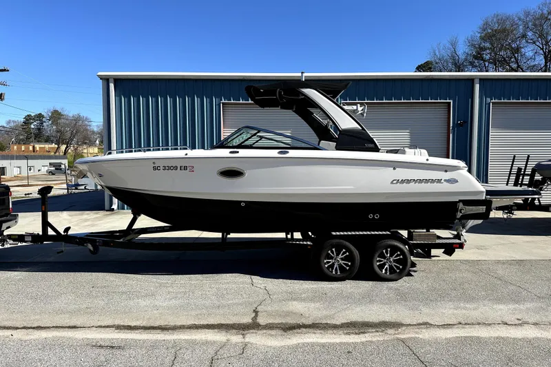 Slide: The Image of 2021 Chaparral 26 Surf boat on trailer, parked outside blue warehouse. - 2