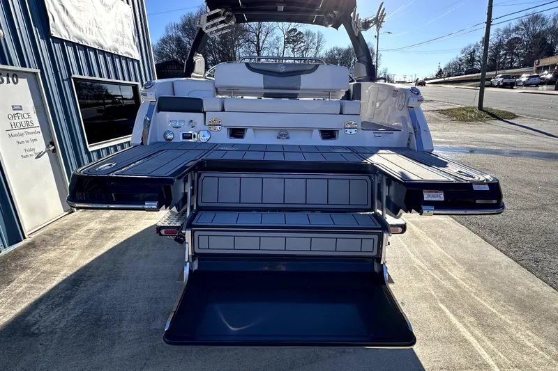 Slide: The Image of 2021 Chaparral 26 Surf boat with extended swim platform and seating, parked outside a building. - 6