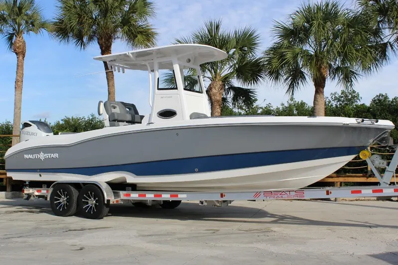 The Image of 2025 NauticStar 251 Hybrid boat on trailer, surrounded by palm trees. - 1