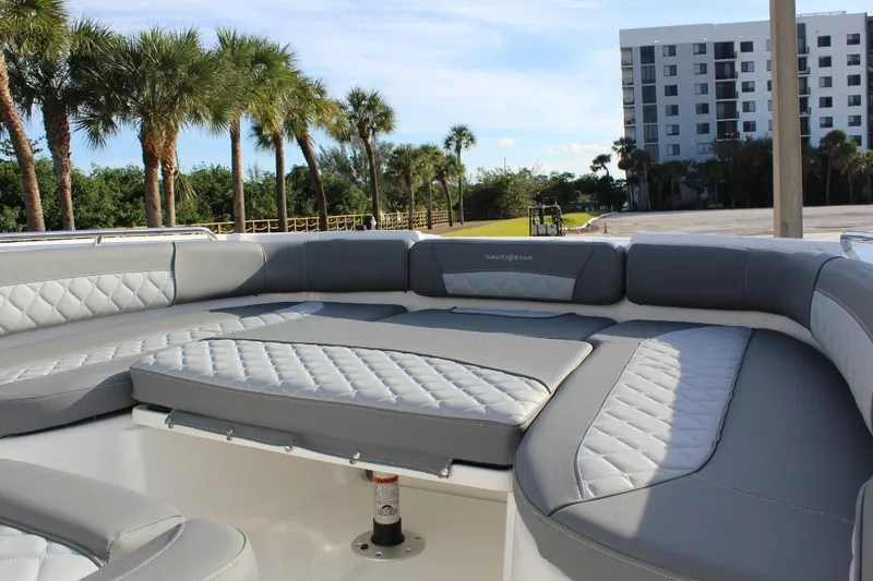 Slide: The Image of 2025 NauticStar 251 Hybrid boat interior with gray cushioned seating, palm trees, and building in background. - 24