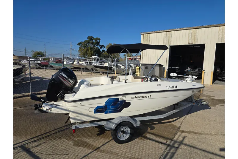 Slide: The Image of 2019 Bayliner Element E16 boat on trailer, parked outdoors near a warehouse. - 6