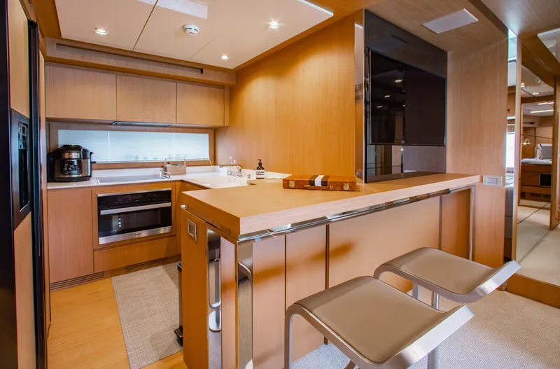Slide: The Image of Modern kitchen interior on a 2016 Riva 88' Florida yacht, featuring sleek wood finishes and bar seating. - 7