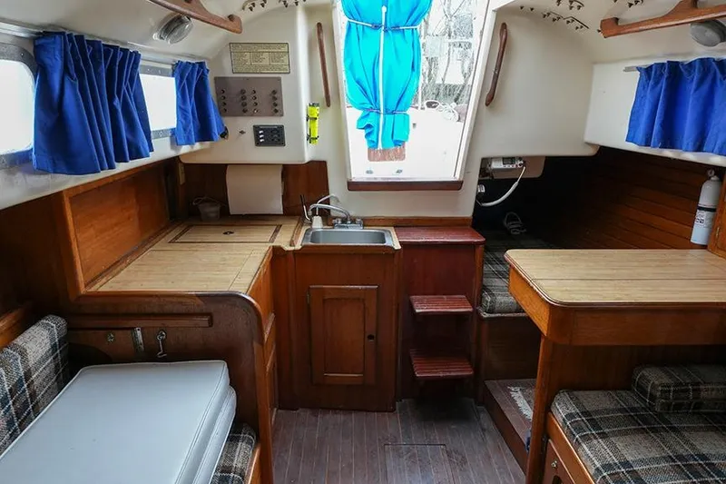 Slide: The Image of Interior of a 1978 Bristol 29.9 sailboat with wooden cabinetry and blue curtains. - 29