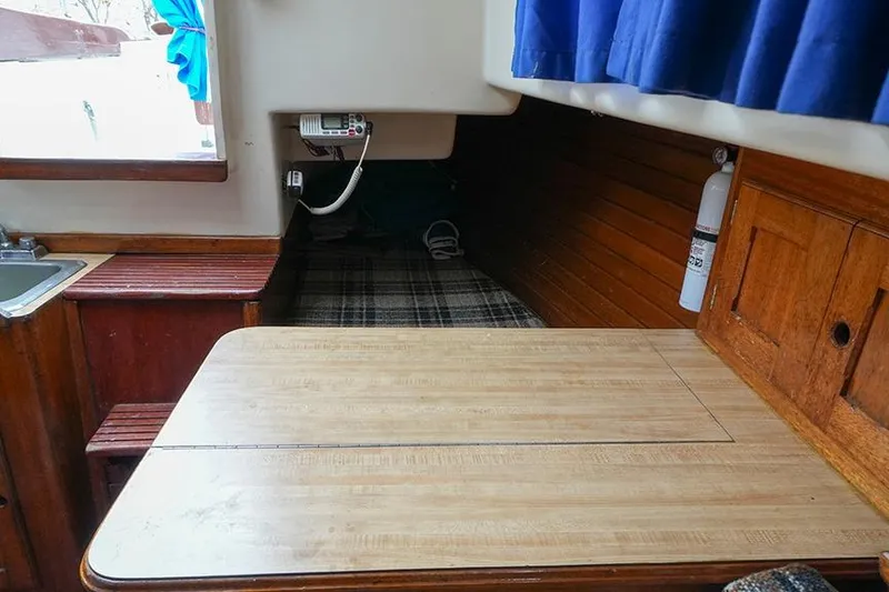 Slide: The Image of 1978 Bristol 29.9 boat interior with wooden table, plaid bedding, and blue curtains. - 34